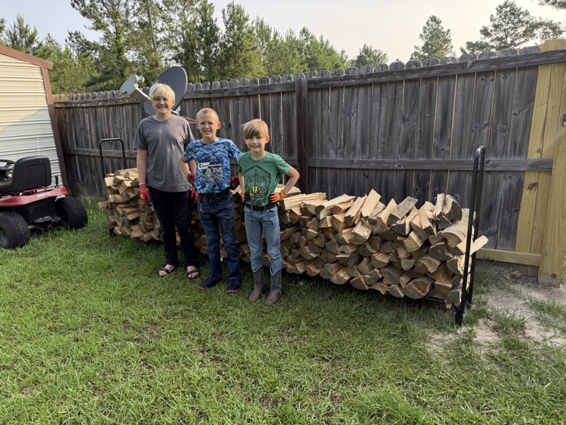 Jeremiah, Ezekiel, and Yosef with a face cord of split wood stacked on a customer's rack.