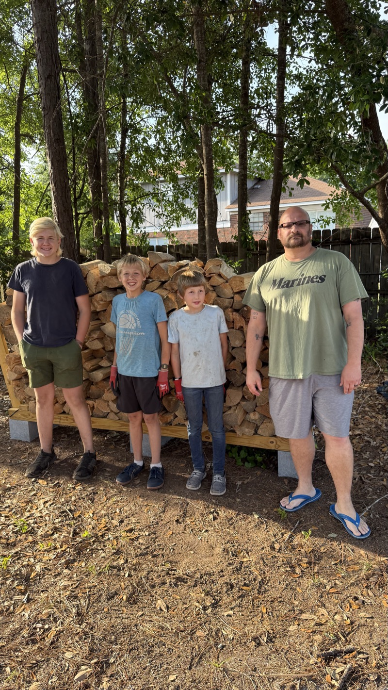 Mr. Warden with the three brothers, beside his built rack and a full face cord of split wood.